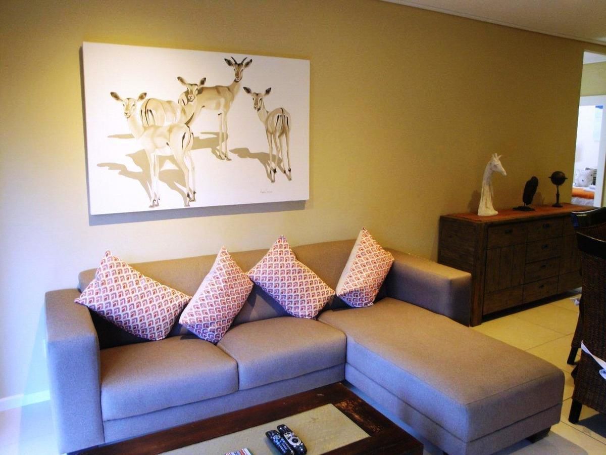 Ein Wohnzimmer mit einem grauen Ecksofa, dekorativen Kissen mit Muster, einem Couchtisch und einem Bild von Hirschen an der Wand.