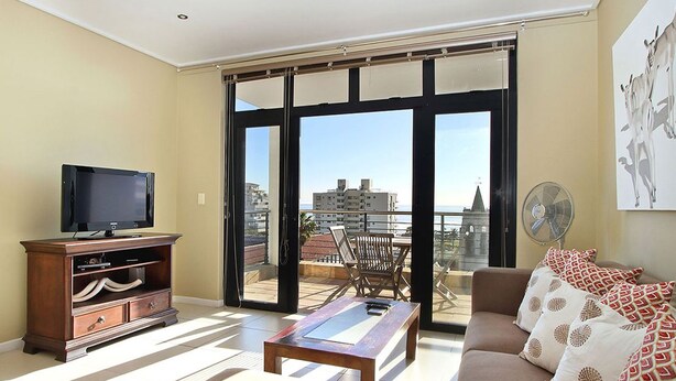 A living room with a television, a coffee table, a sofa, and a balcony with a view of buildings. - Atlantic Views 6 (Cape Town)