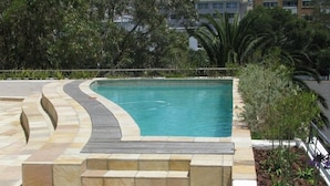 A swimming pool with a curved edge, surrounded by a stone deck and steps leading into the water. - Atlantic Views 6 (Cape Town)