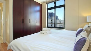 A bedroom with a large bed, a wardrobe, and a window with a view of buildings. - Atlantic Views 6 (Cape Town)