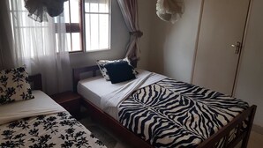 A bedroom with a bed, a window with curtains, a wardrobe, and a hanging decorative item. - Mubwiza Courts (Kigali)