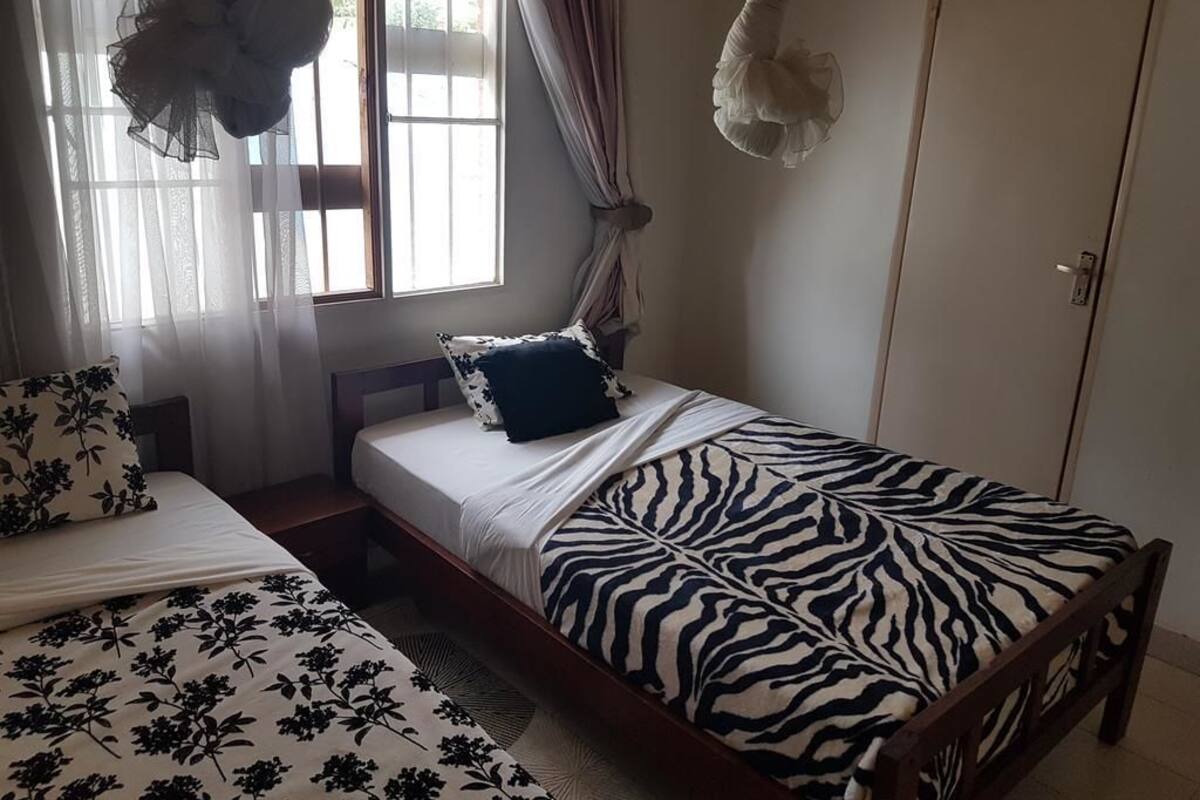 A bedroom with a bed, a window with curtains, a wardrobe, and a hanging decorative item.