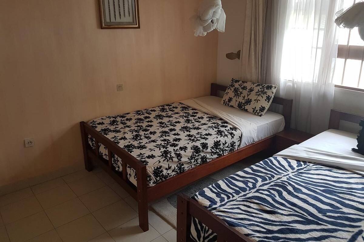 A bedroom with a single bed, a bedside table, a nightstand, a window with curtains, and a framed picture on the wall.