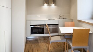 Une cuisine compacte dotée d’un four encastré, d’une hotte en acier inoxydable et d’une table à manger en bois avec des chaises.