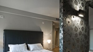 Une chambre à coucher avec un grand lit, une table de chevet, une lampe et un mur orné d’un motif floral.