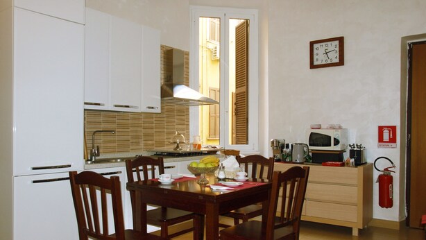 Cocina compacta con armarios blancos, una mesa de comedor con cuatro sillas, microondas y extintor.