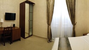 Una habitación de hotel con cama, escritorio, silla, televisor y un espejo grande.