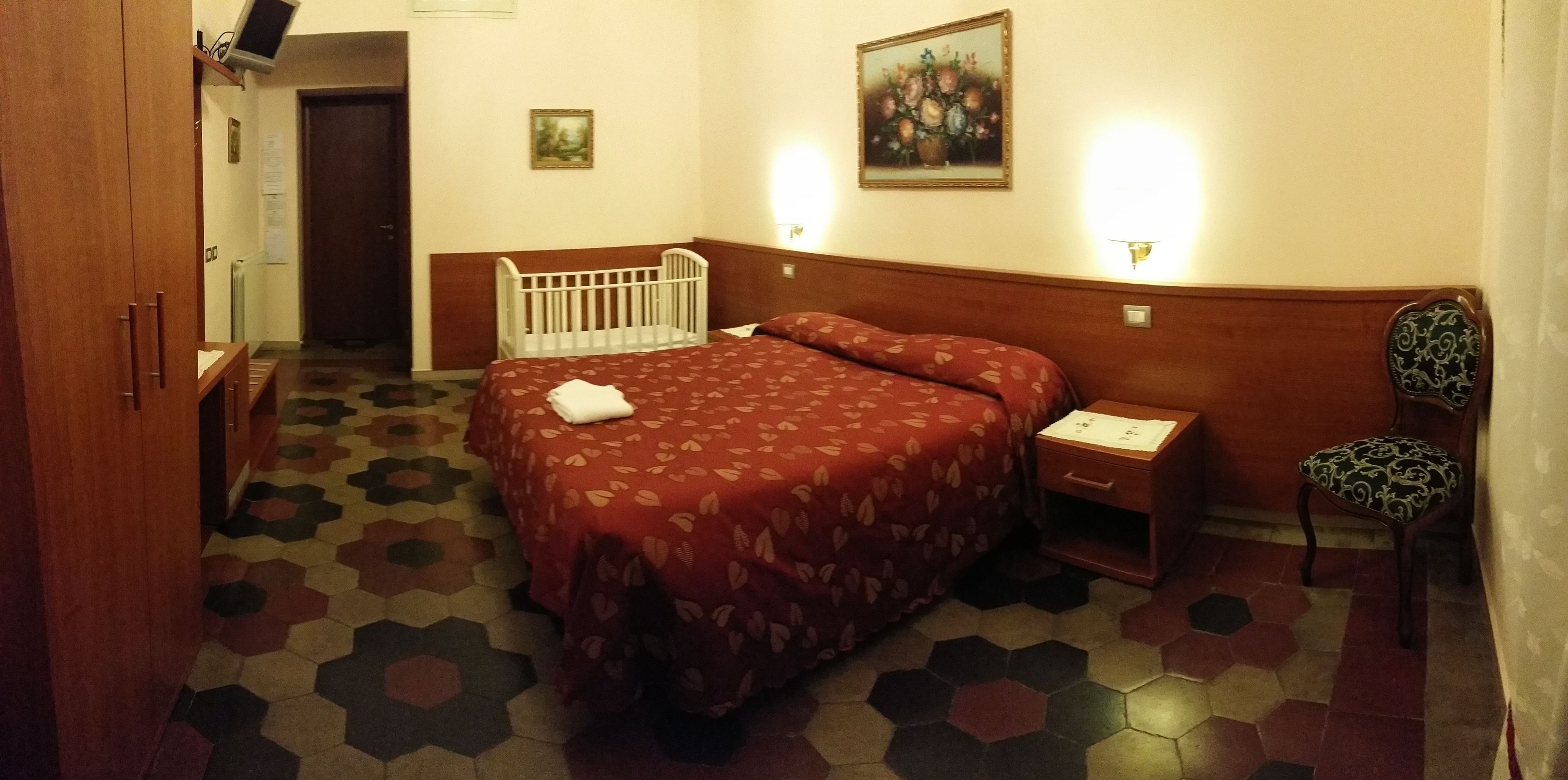 Une chambre d’hôtel comprenant un lit, une table de chevet, une chaise, une armoire en bois, une porte et un sol à motifs.