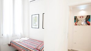 Una habitación con cama, ventana con cortinas, aire acondicionado y dos cuadros en la pared.