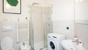 Un baño moderno con cabina de ducha de vidrio, lavadora, lavamanos e inodoro.