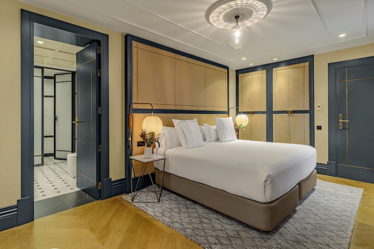Une chambre d’hôtel moderne avec un grand lit, des tables de chevet, un luminaire au plafond et une vue sur la salle de bain.