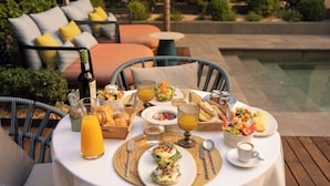 A table set for breakfast with croissants, fruit, and coffee, overlooking a pool.