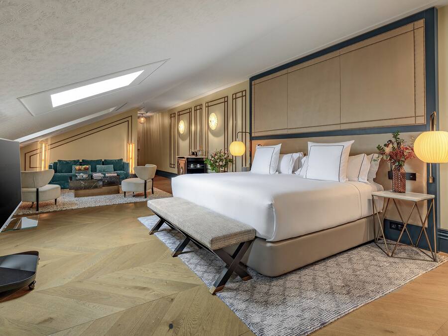 Un dormitorio moderno con una cama grande, un banco, un televisor y un sofá.