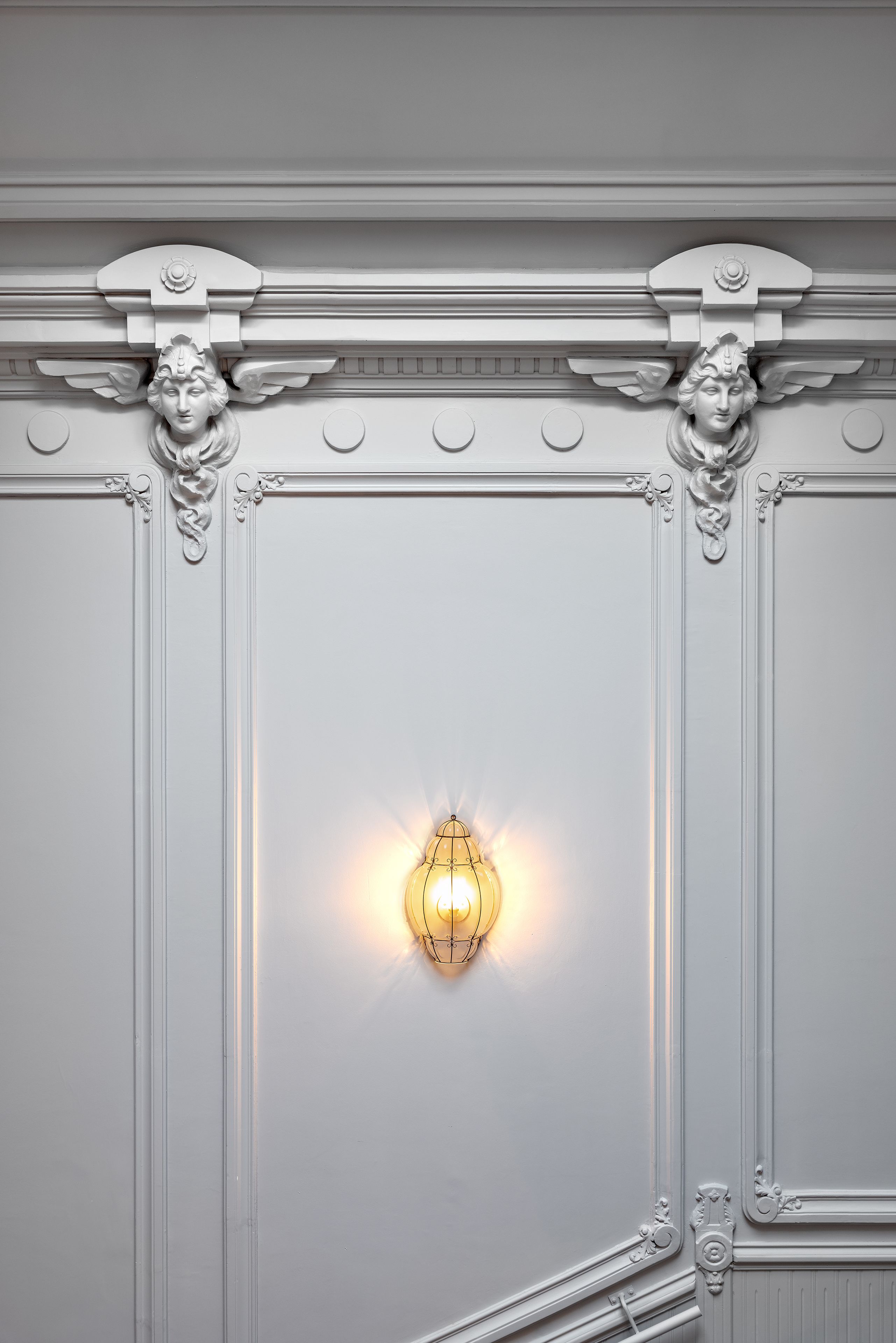 A wall with ornate moldings and a wall sconce.