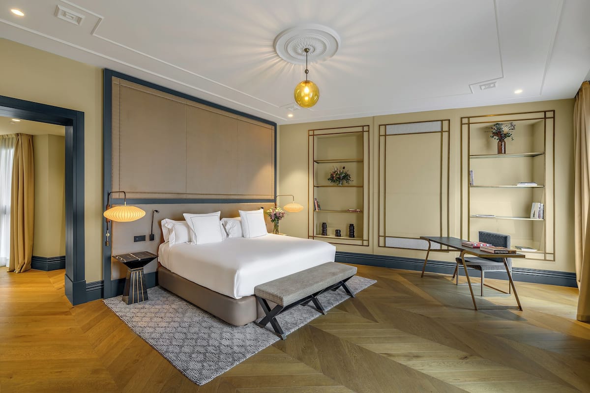 Une chambre d’hôtel moderne dotée d’un grand lit, de tables de chevet, d’un bureau et d’étagères intégrées.