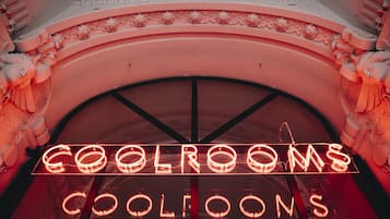 A neon sign spelling "COOLROOMS" in a stylized font, set against a curved architectural backdrop with ornate details.
