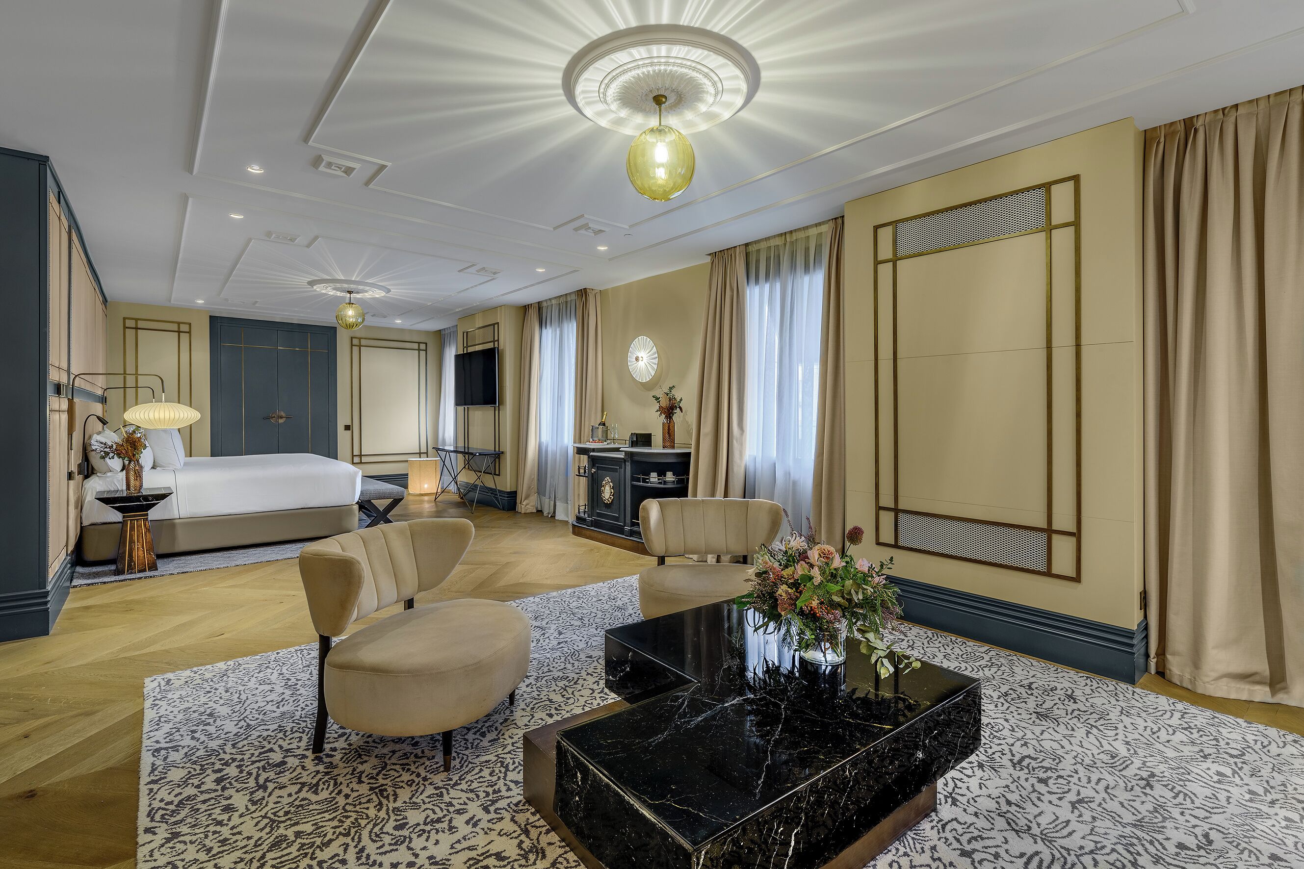 Een hotelkamer met een bed, twee fauteuils, een salontafel, een televisie en een decoratieve vaas.