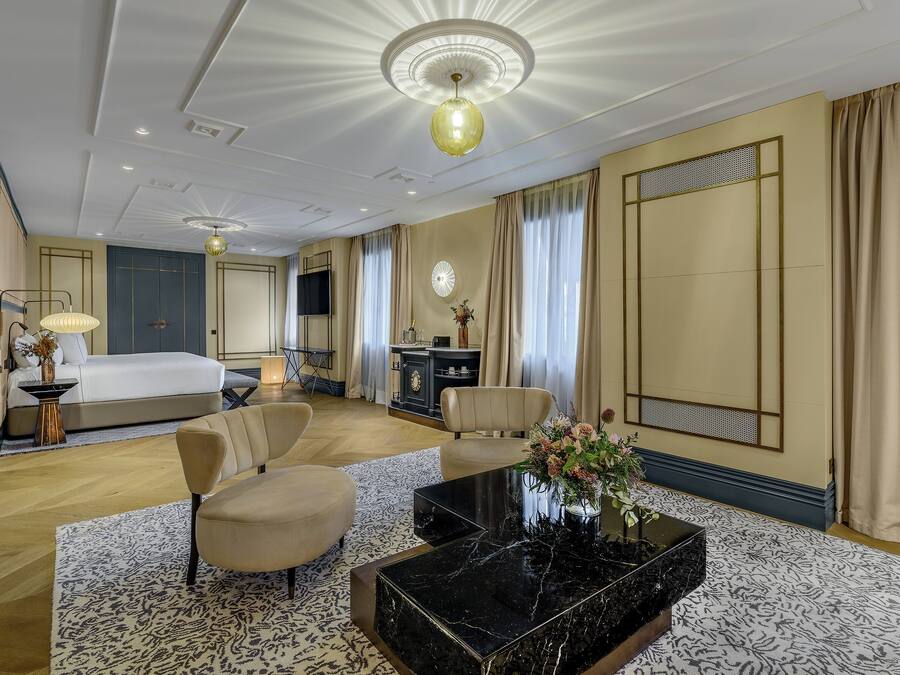 Een hotelkamer met een bed, twee fauteuils, een salontafel, een televisie en een decoratieve vaas.