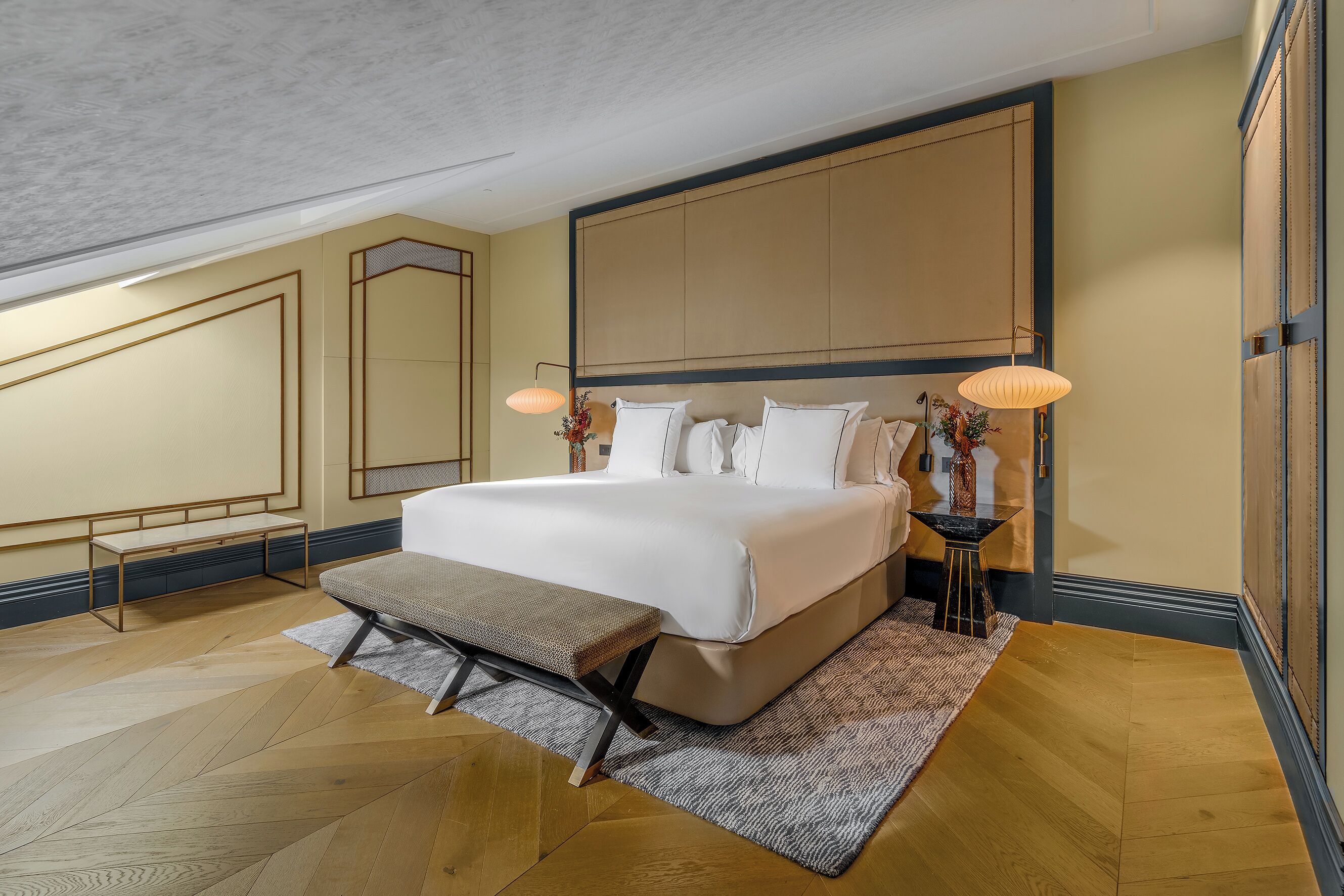 Un dormitorio moderno con una cama grande, mesitas de noche, un banco y un espejo.