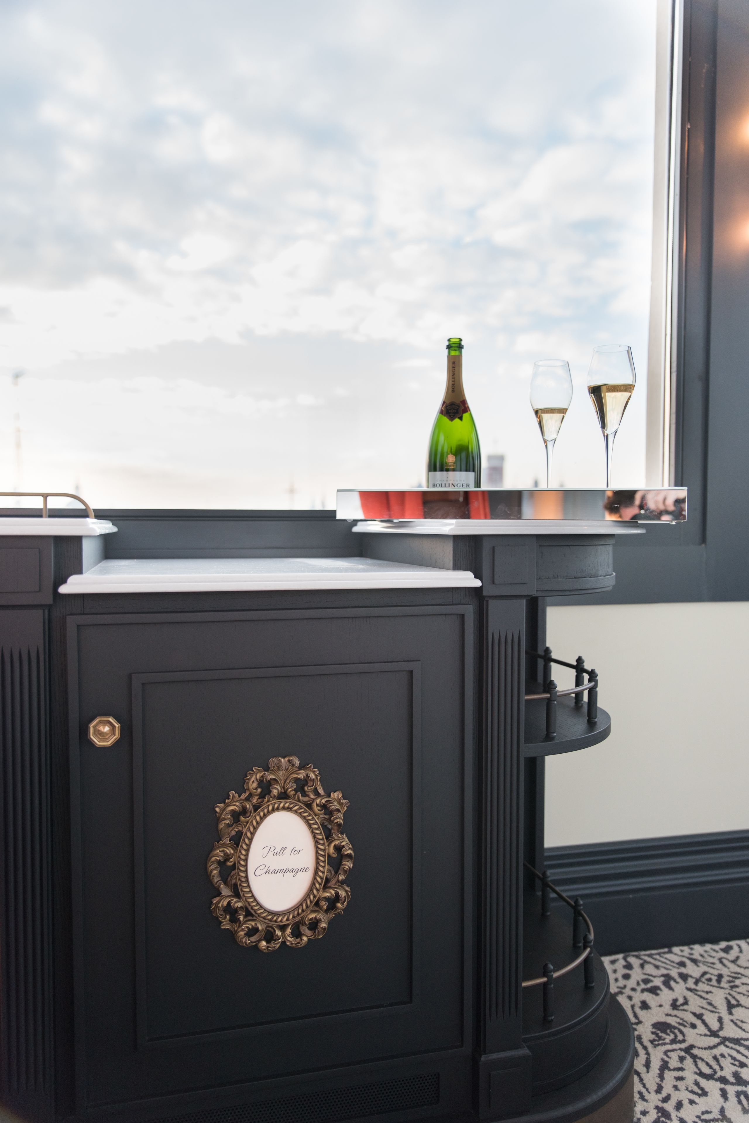 Un minibar negro con una botella de champán y dos copas sobre una bandeja.