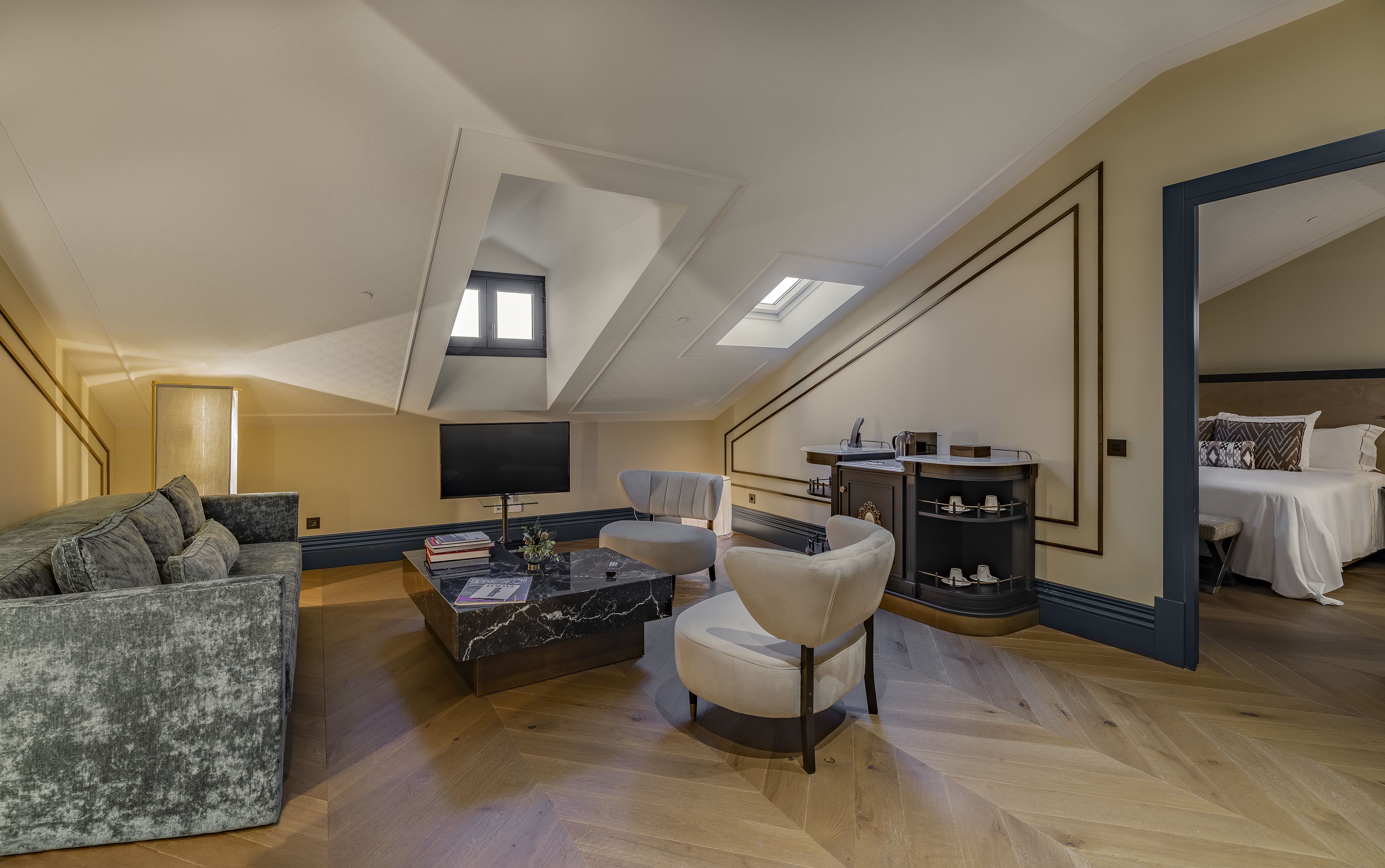 A spacious loft bedroom with a large bed, a seating area with a sofa and armchairs, a TV, and a small kitchen area.