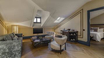 A spacious loft bedroom with a large bed, a seating area with a sofa and armchairs, a TV, and a small kitchen area.