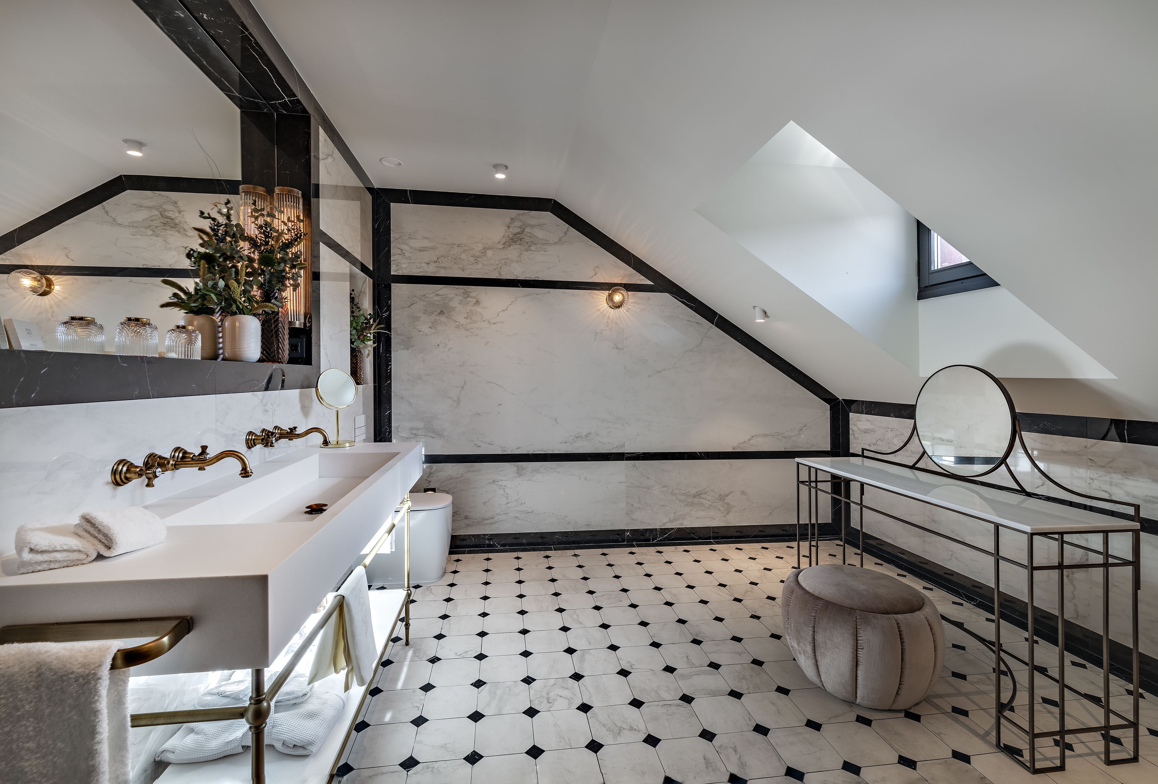 Een moderne badkamer met een vloer van wit marmer, een grote spiegel, een wastafel met een gouden kraan en een plant in pot.