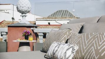 A rooftop terrace with a sofa, pillows, a table with a drink and flowers, and a decorative globe.
