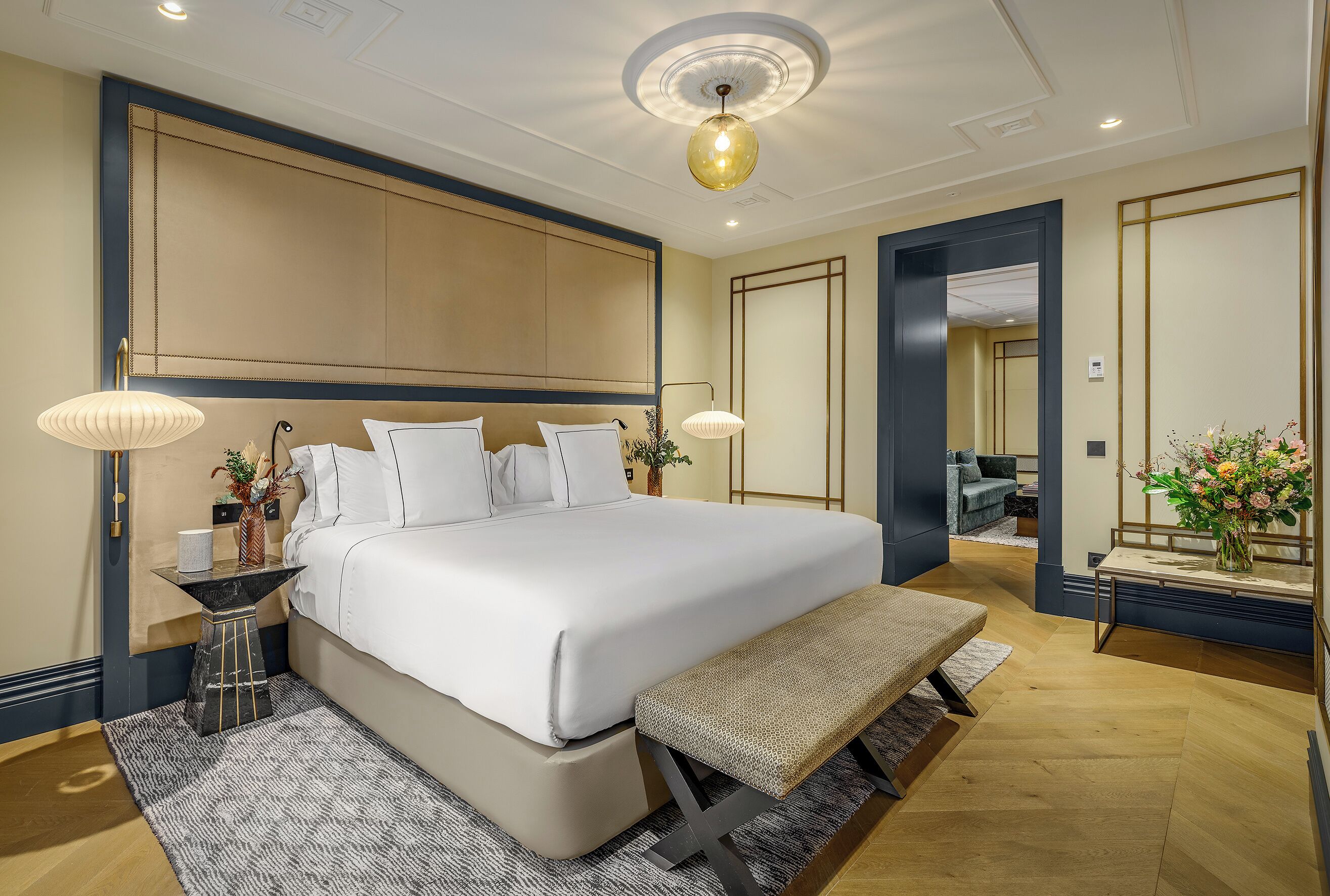 Een moderne hotelkamer met een groot bed, bedlampjes, een bankje, een tafeltje en een spiegel.