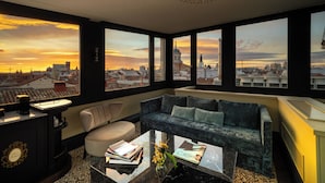 Een moderne woonkamer met een groot raam dat uitzicht biedt op de stad bij zonsondergang.