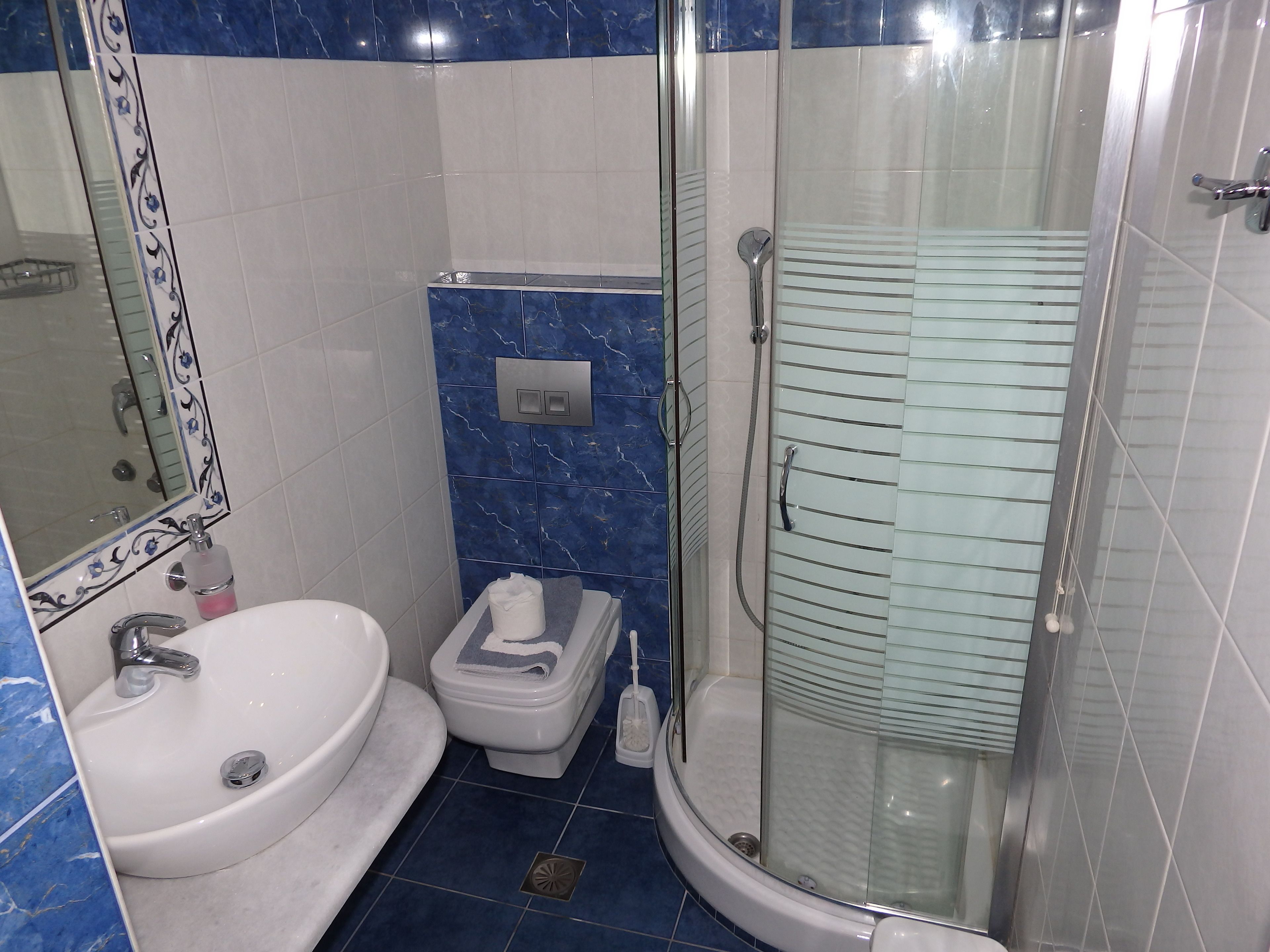 Un baño con lavamanos blanco, inodoro y ducha con mampara de vidrio.