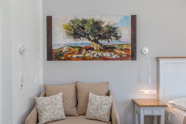Un dormitorio con un sofá color beige, una mesita de noche pequeña y un cuadro de un árbol en la pared.