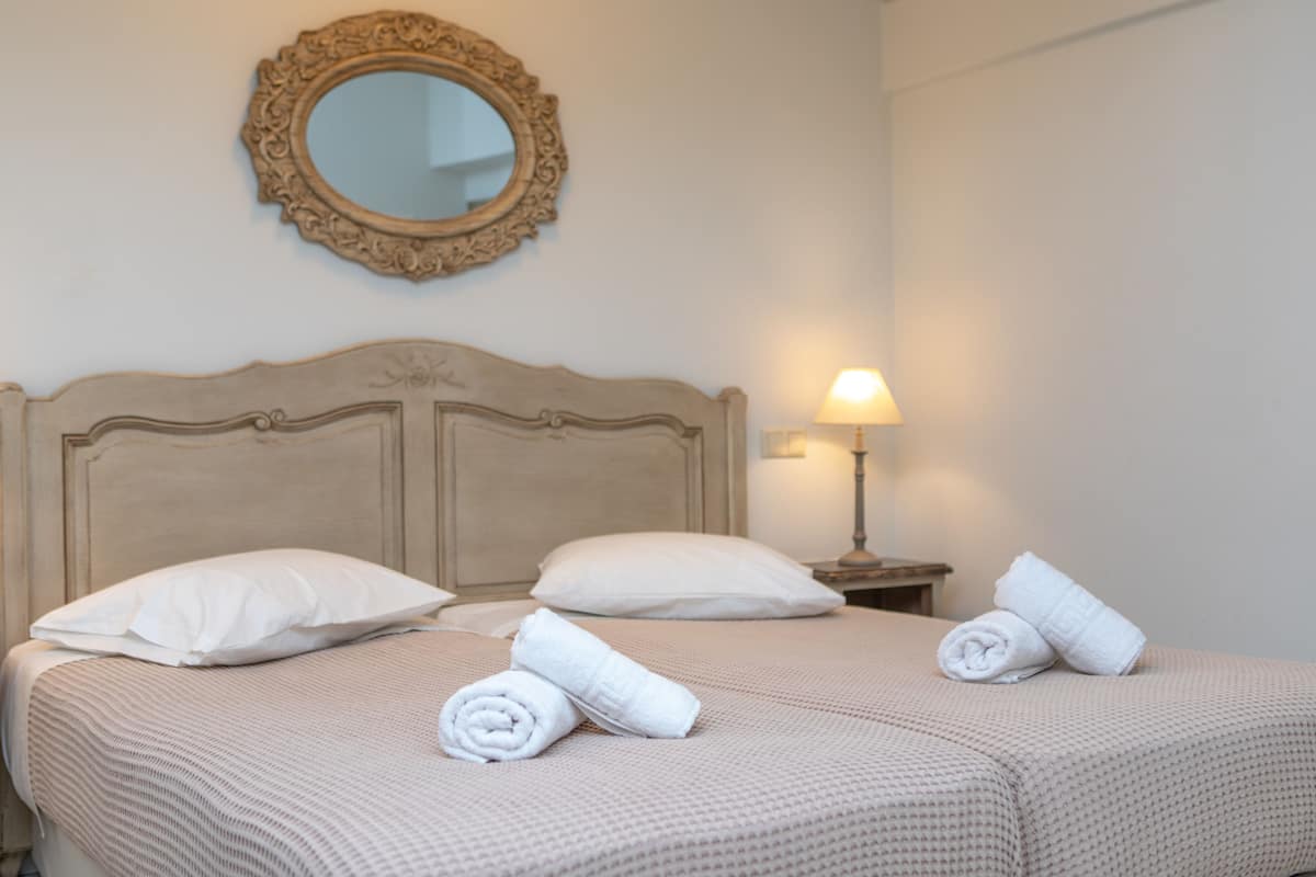 A neatly made bed with two pillows and rolled towels, a bedside lamp, and a mirror on the wall.