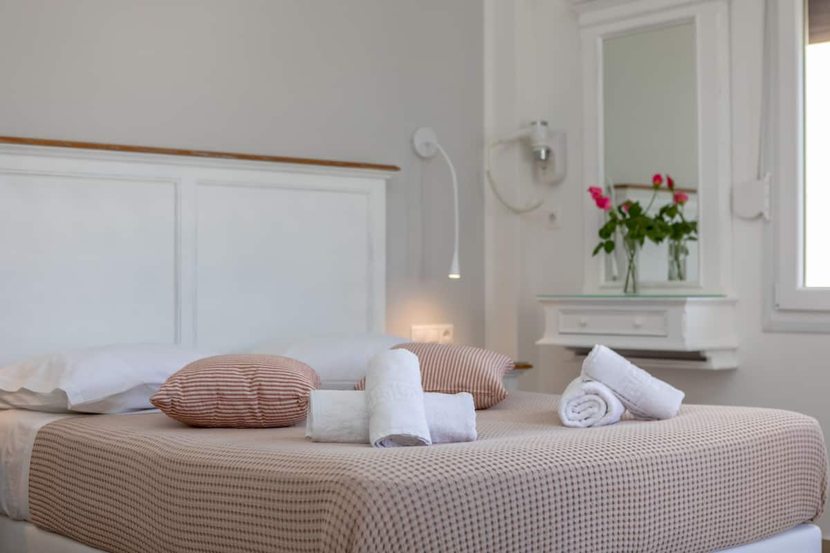 A neatly made bed with a patterned bedspread, a wooden headboard, and a bedside table with a vase of flowers.