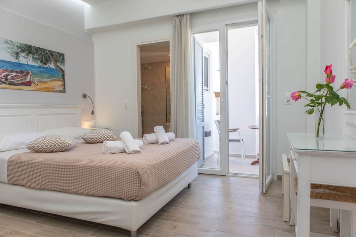 A bedroom with a bed, a desk, and a chair. There is a painting on the wall and a vase with flowers on the desk.
