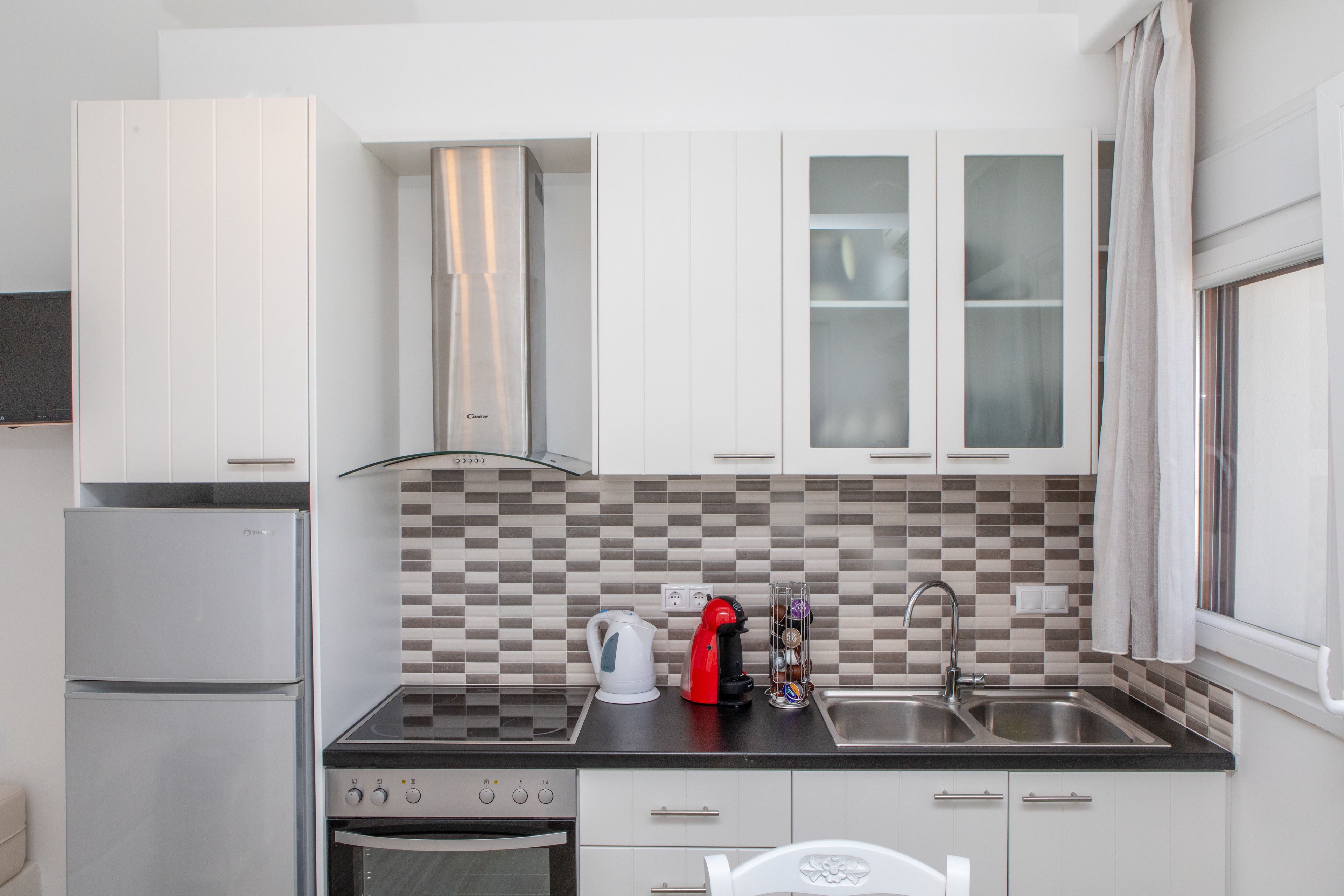 Una cocina moderna con armarios blancos, encimera negra, refrigerador de acero inoxidable, estufa y fregadero.