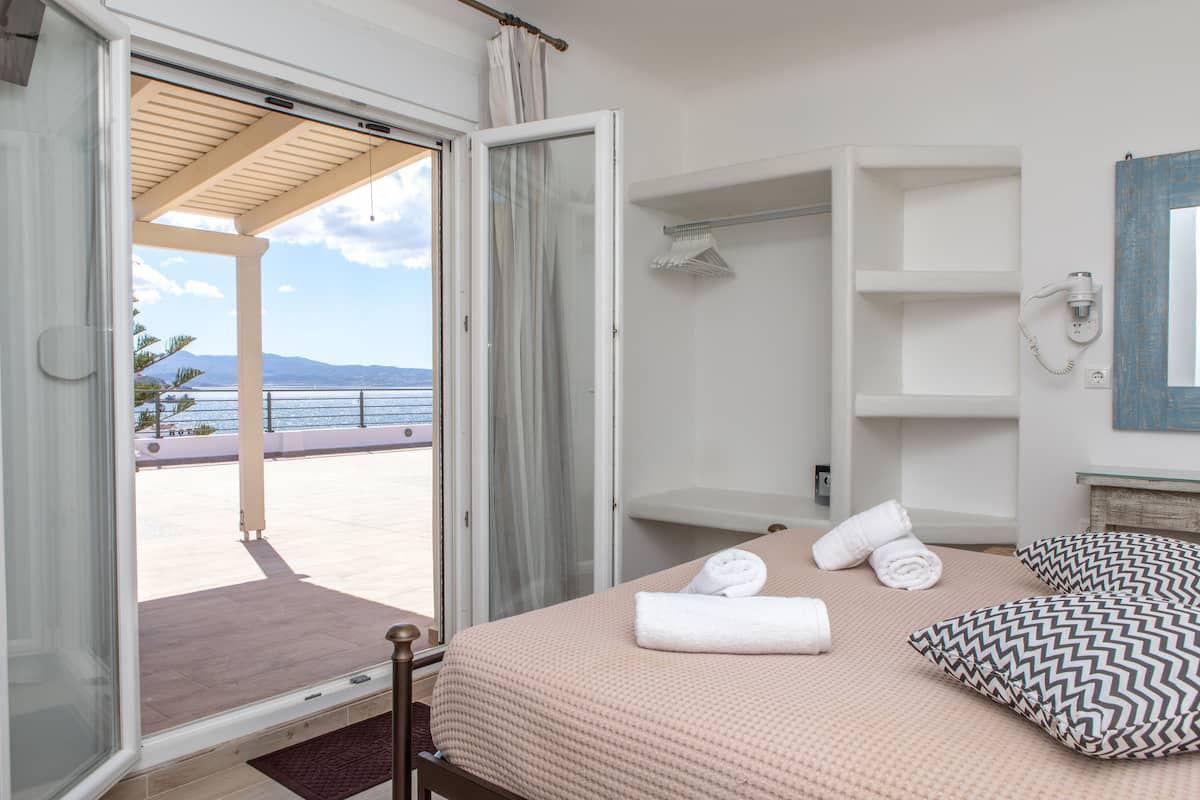 A bedroom with a bed, pillows, a bathroom with a shower, and a view of the sea.