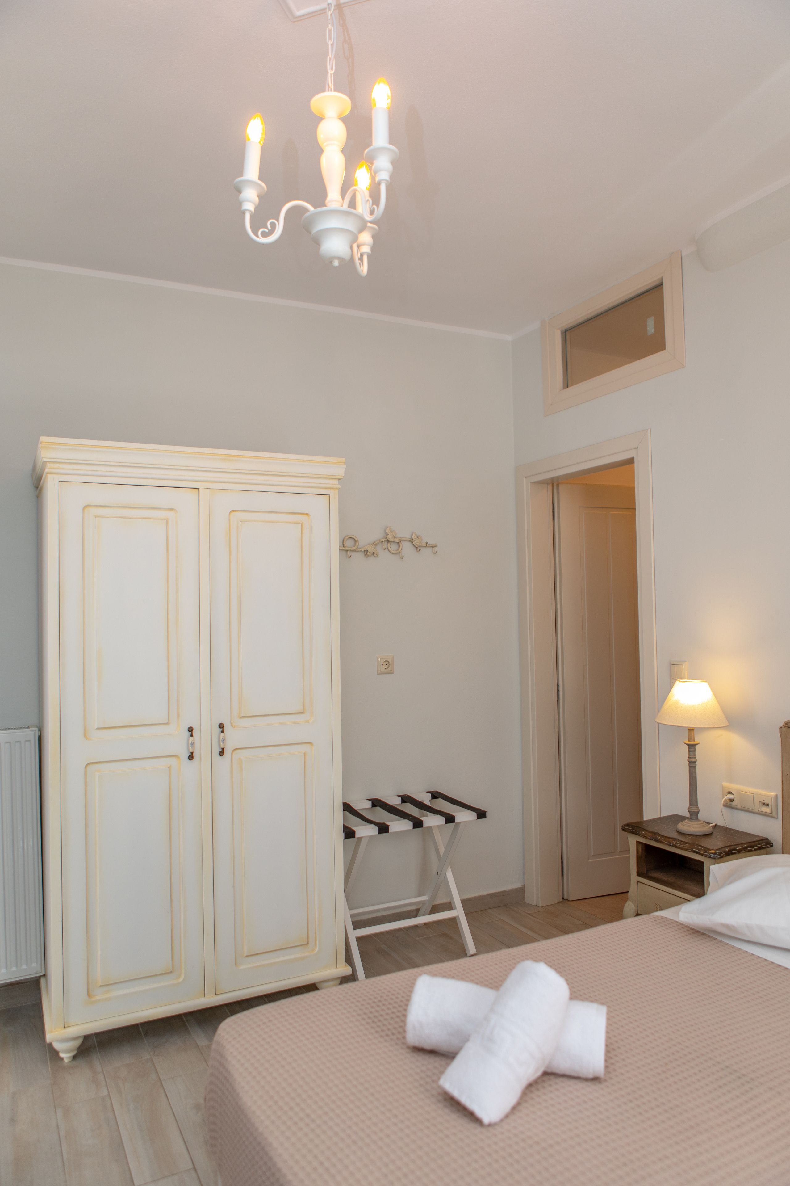 Una camera da letto con un letto, un armadio, una sedia a dondolo, un comodino con una lampada e una porta che dà su un'altra stanza.