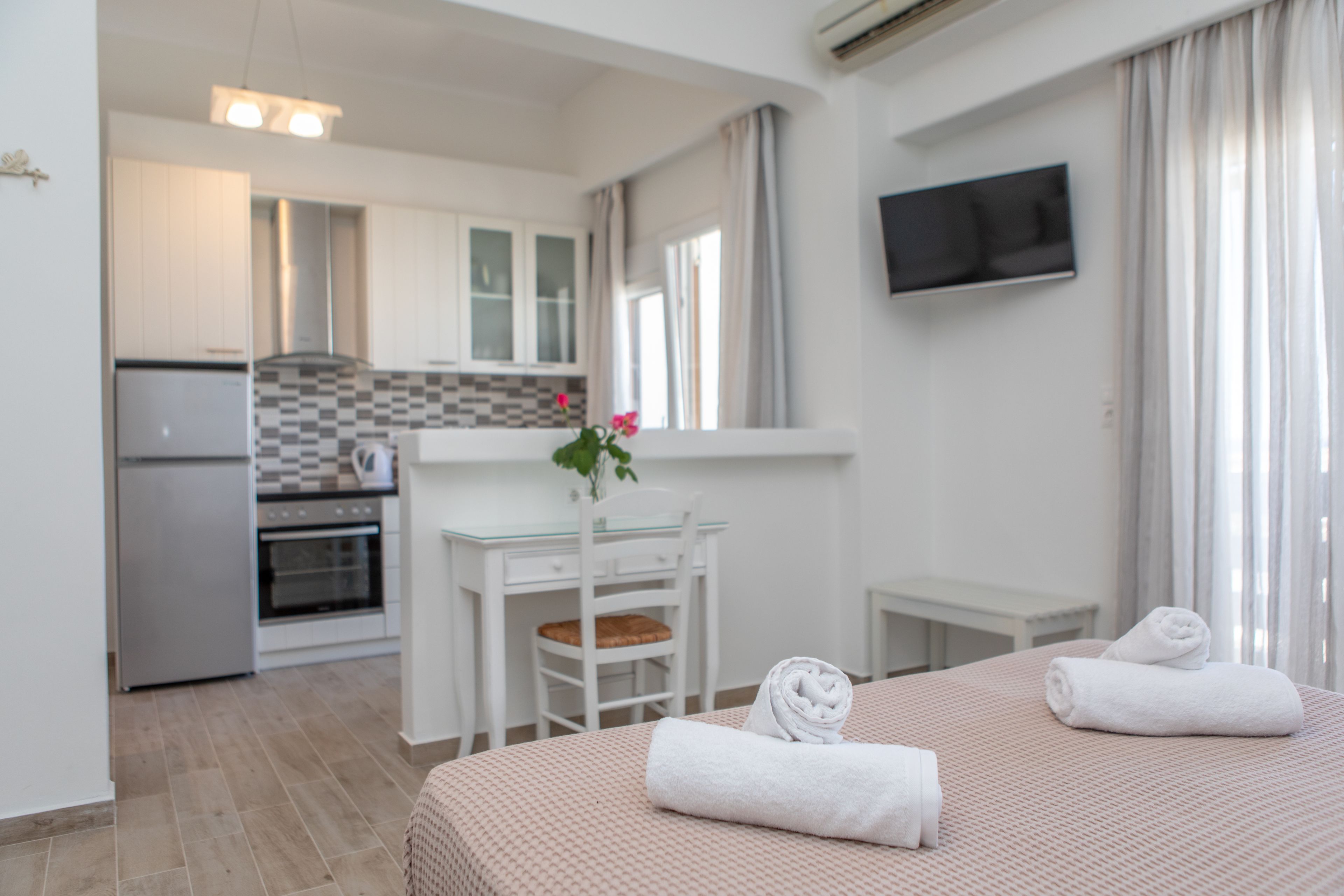 A hotel room with a bed, a desk, a chair, a TV, and a kitchen area.