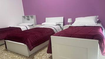 Camera d'albergo con due letti, ognuno con testata bianca e copripiumino viola. Su ogni letto, un comodino con una lampada.