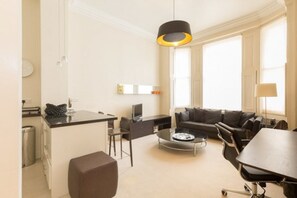 A modern living room with a sofa, coffee table, and dining table. There is a kitchen area with a counter and a sink.