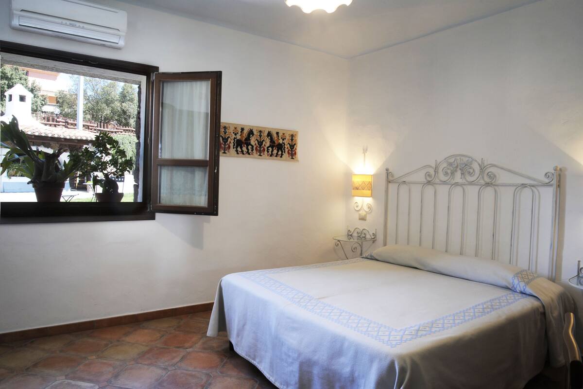 Une chambre à coucher avec un lit, une fenêtre donnant sur des immeubles, un climatiseur fixé au mur et un élément décoratif mural.