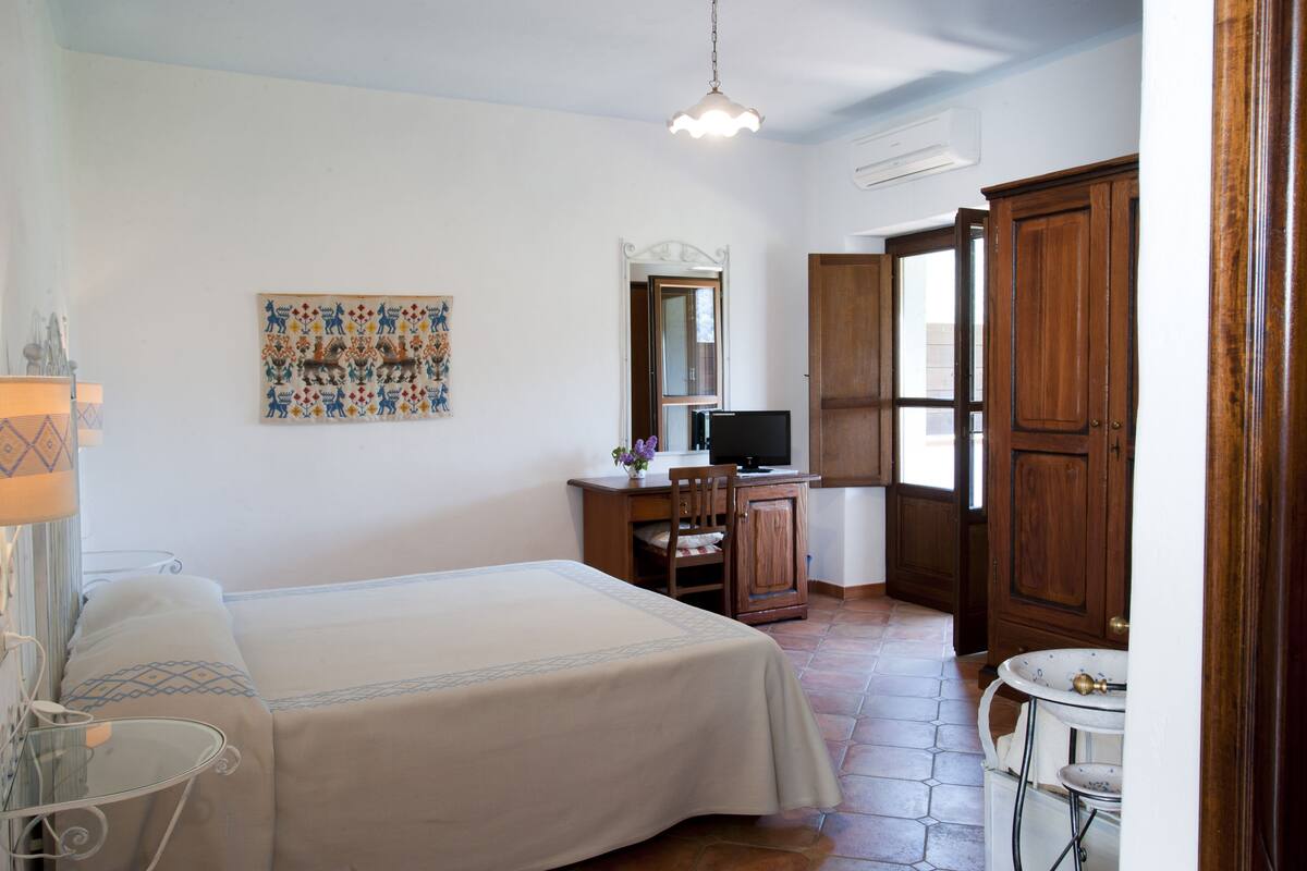 Une chambre d’hôtel avec un lit, un bureau avec un ordinateur, un miroir et une porte en bois.