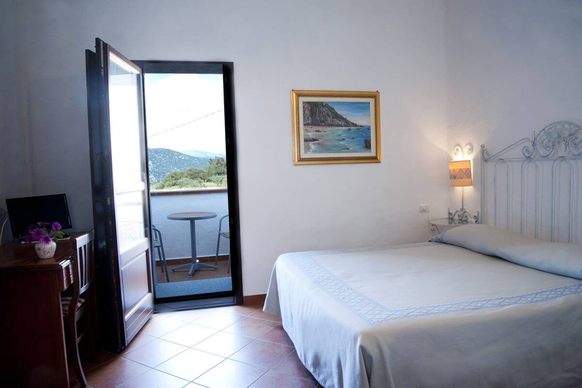 Une chambre d’hôtel avec un lit, un tableau, une table avec des chaises et une vue sur l’extérieur.