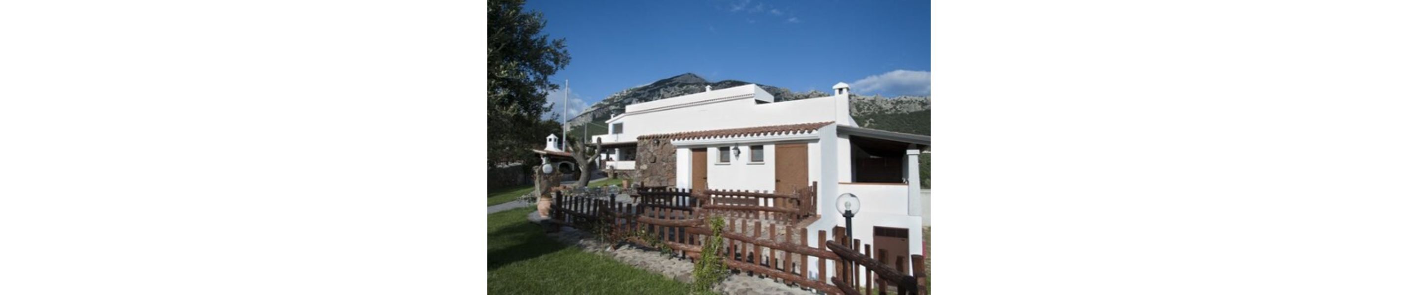 Um edifício branco com cerca marrom, uma pequena torre e uma montanha ao fundo.