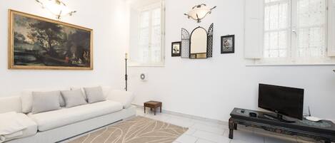 A modern living room with a white sofa, a large painting, a flat-screen TV, and a patterned rug.