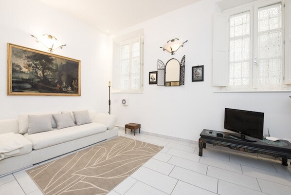 A modern living room with a white sofa, a large painting, a flat-screen TV, and a patterned rug. - Pergola 48 (Florence)