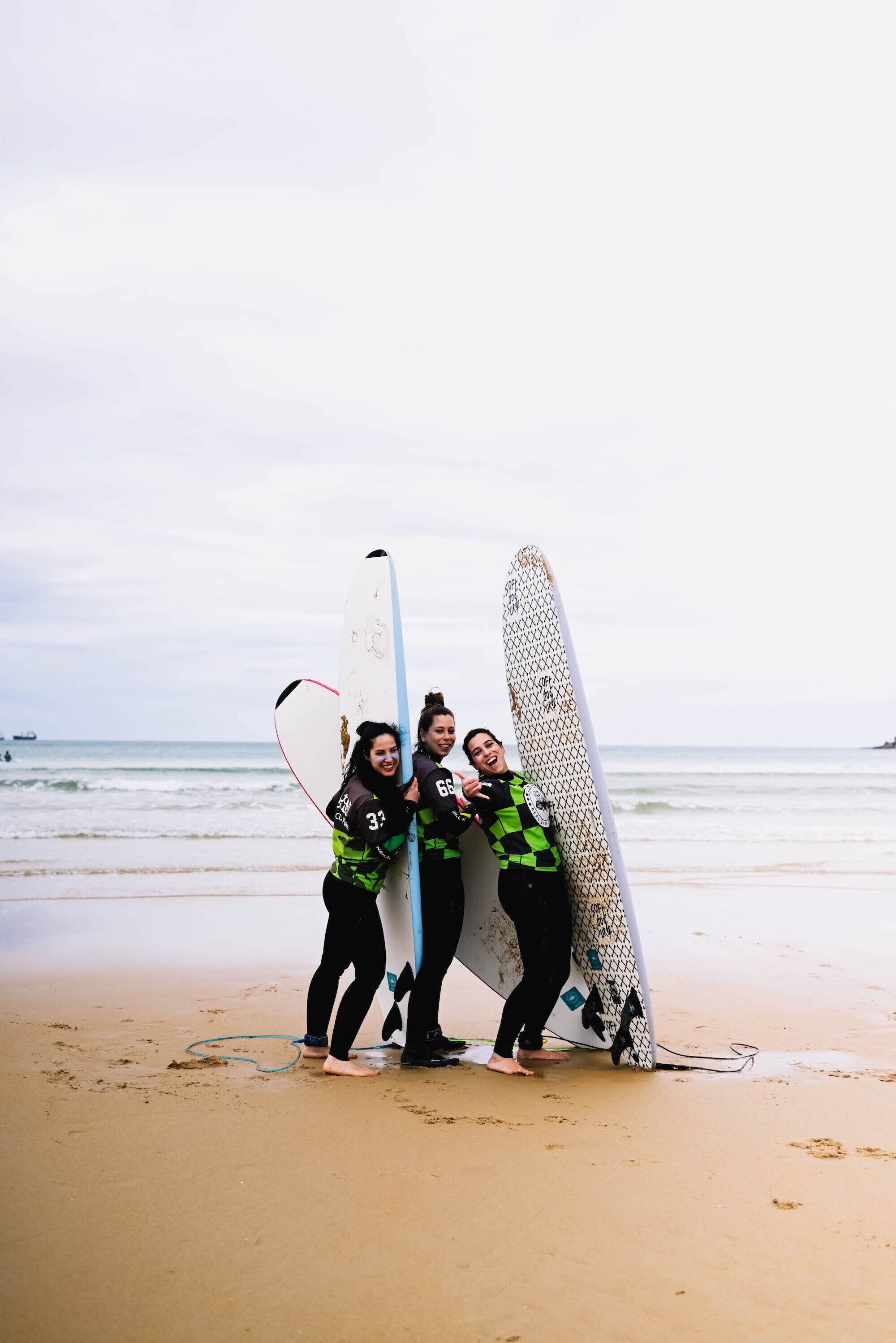 Three people standing on a sandy beach holding surfboards.