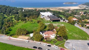 An aerial view of a coastal property with a large building, a parking lot, and a beach in the background. - Latas Surf House (Ribamontan al Mar)