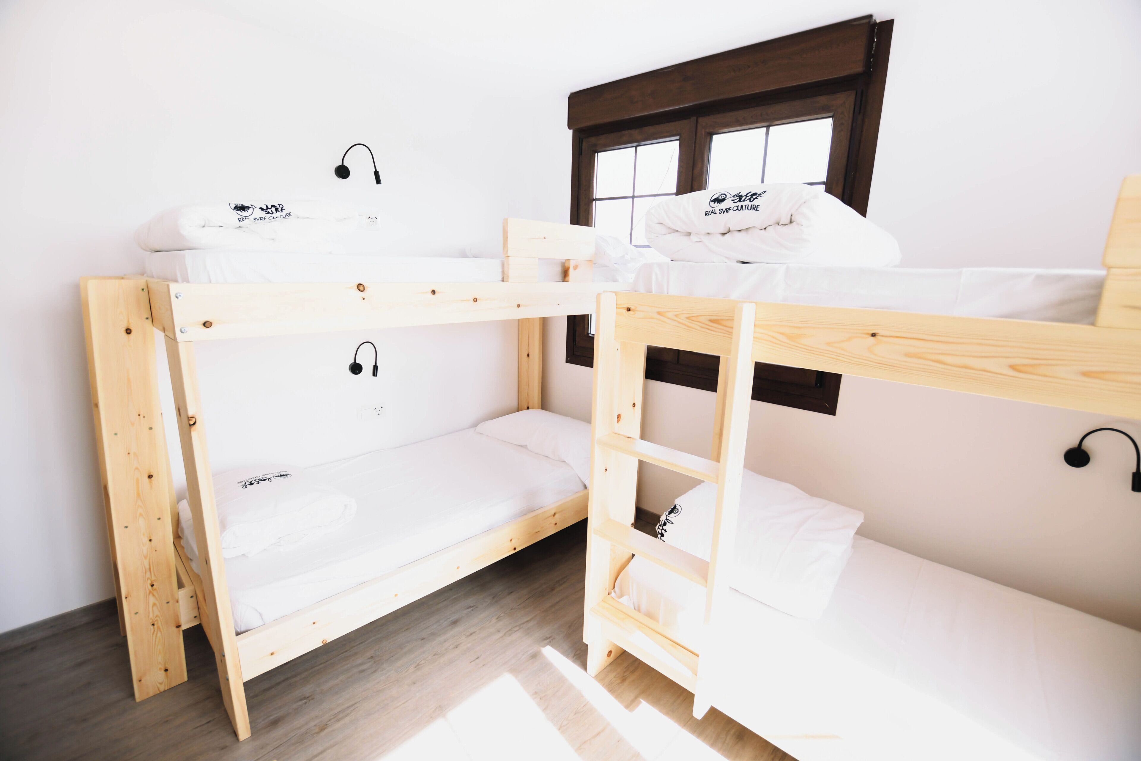 Habitación con literas, ventana, suelo de madera y pared blanca.